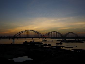 Silhouette bridge over river against sky during sunset