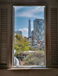 Trees and buildings against sky seen through glass window