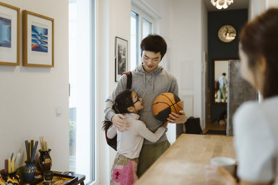 Brother holding basketball and embracing sister while standing at home