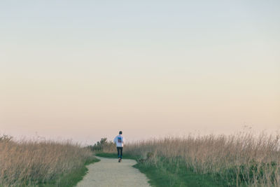 Rear view of man walking on field against clear sky