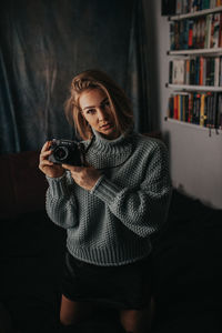 Portrait of woman holding camera at home