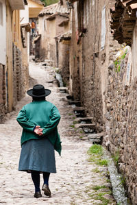 Full length rear view of woman walking on pathway amidst houses