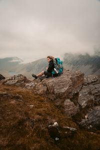 Man sitting on rock against sky