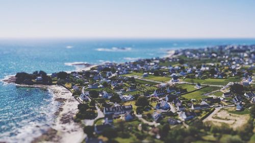 Tilt-shift image of townscape by sea against clear sky