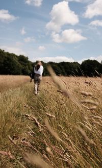 Rear view of woman walking on field against sky