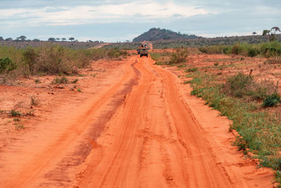 A safari vehicle on a dirt road against  mountains at the tsavo east national park in kenya