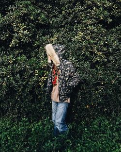 Woman in hooded jacket standing against plants