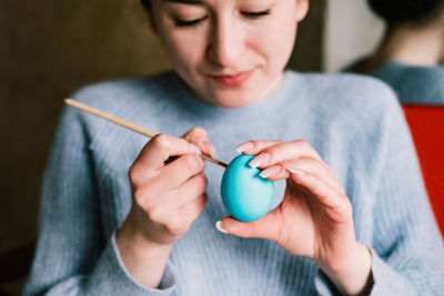 Close-up of young woman painting egg while sitting at home