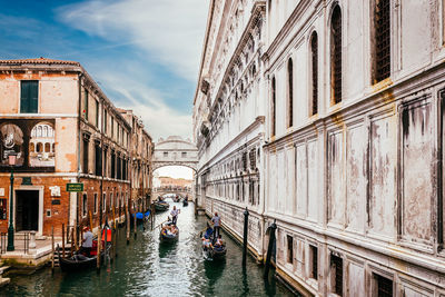 Boats in canal amidst buildings against sky