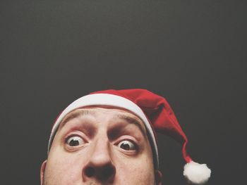 Cropped image of surprised man wearing santa hat against black background