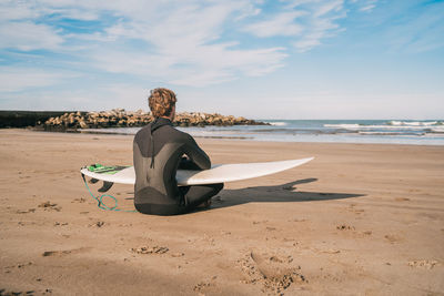 Man sitting on sand at beach against sky