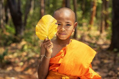 Portrait of smiling boy holding leaf while standing against trees in forest