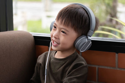 Close-up of boy wearing headphones while sitting against brick wall