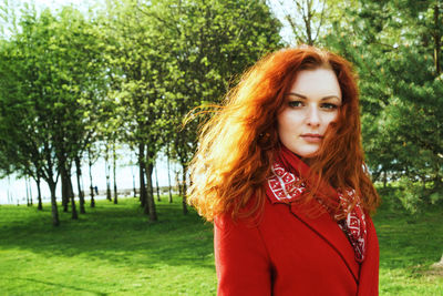 Portrait of a cute woman in a red coat against the background of a green park