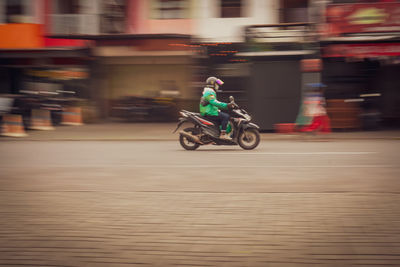 Blurred motion of man riding motor scooter on street