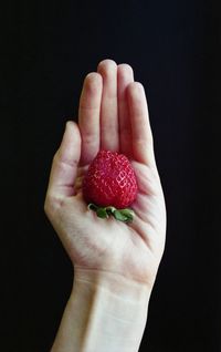 Close-up of hand holding strawberry over black background