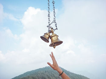 Cropped hand of woman reaching bells against sky