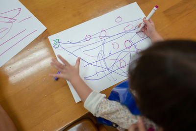 High angle view of girl writing over paper on table