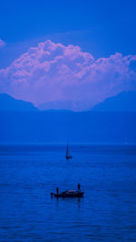 People sailing in sea against sky at dusk