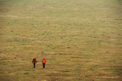 Rear view of two people walking on field