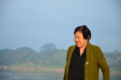 Senior woman standing at lakeshore against sky