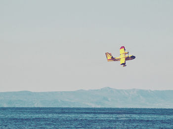 Firefighting aircraft flying over sea against clear sky