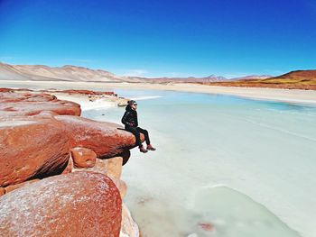 Young woman standing on rock against clear blue sky