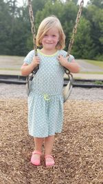 Portrait of girl smiling while standing with swing at playground