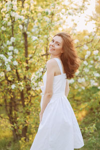 A cute happy young woman with a hairstyle in a white dress is walking enjoying nature in the summer