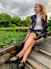 Beautiful young woman sitting in park against sky
