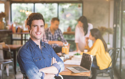 Portrait of businessman smiling while working with coworkers in cafe