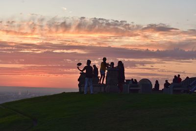 People standing on land against sky during sunset