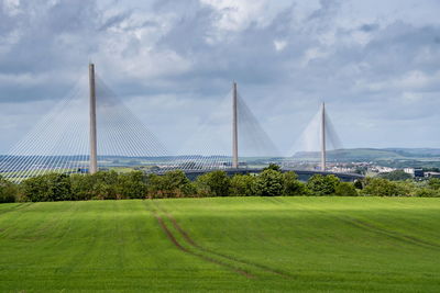 Scenic view of grassy field by bridge against sky