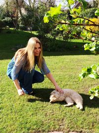 Portrait of woman petting cat lying on grassy field at park