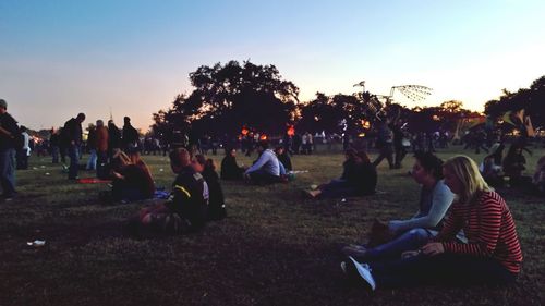 People relaxing on field against clear sky