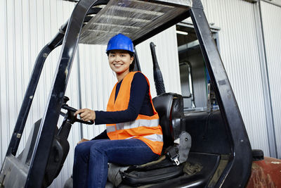 Portrait of confident female worker on forklift in factory