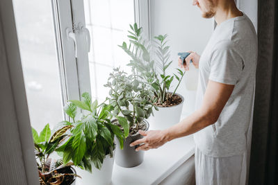 Midsection of man watering potted plants at home