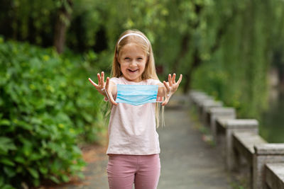 Happy little girl takes off protective medical mask from face outdoors. victory over coronavirus