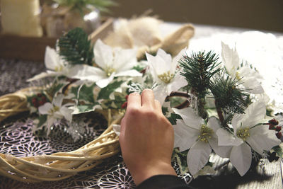 Cropped hand preparing flower wreath on table