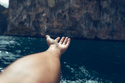 Cropped hand over sea against mountain