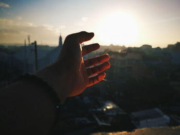 Cropped hand of man against sky during sunset