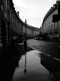 Wet footpath amidst buildings in city