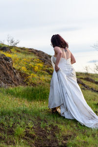 Rear view of woman in wedding dress standing on field against sky