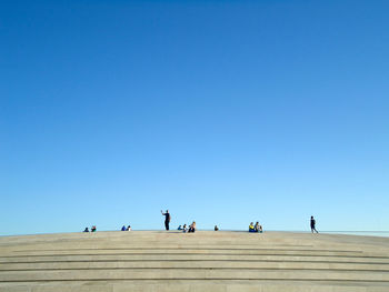 Low angle view of people against clear blue sky