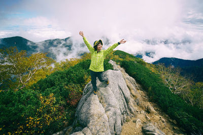Woman with arms raised standing on mountains against sky