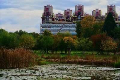 Trees by river against buildings in city during autumn