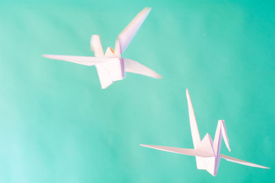 Origami cranes in mid-air against turquoise background