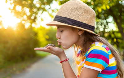 Side view of young woman blowing bubbles while standing outdoors