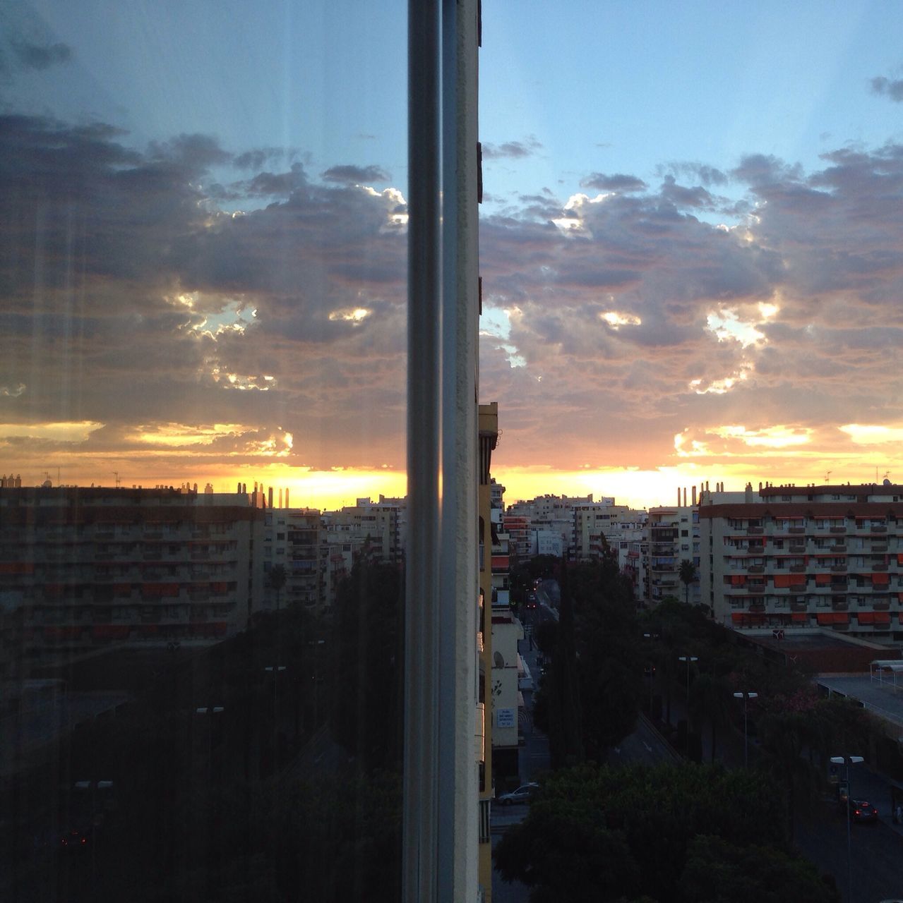 sunset, building exterior, architecture, city, sky, built structure, cityscape, orange color, window, cloud - sky, glass - material, transparent, residential building, residential district, cloud, sun, residential structure, silhouette, sunlight, indoors