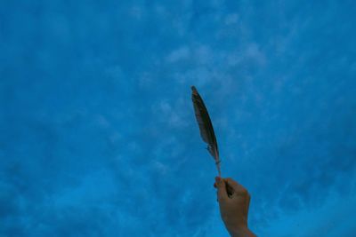 Cropped hand of woman holding feather against blue sky
